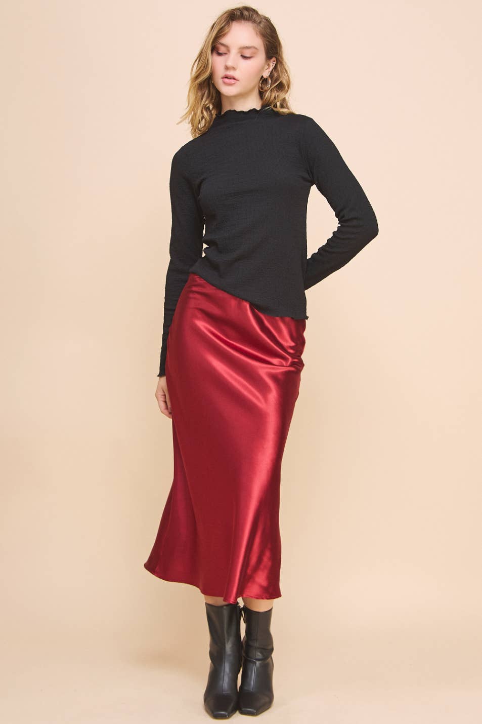Woman wearing a black top and red satin skirt on a beige background